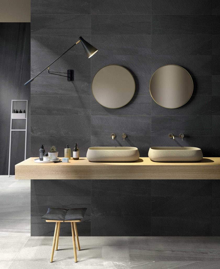image showing active surfaces porcelain tiles in a bathroom, with a pale grey tile on the floor and a darker grey tile used on the walls. the bathroom has a wooden counter and two sinks, with mirrors above, as well as a lamp attached to the wall