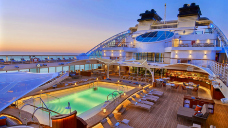 the top deck of seabourn ovation during sunset, featuring a lit up pool surrounded by many chaise loungers